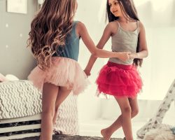 Two happy little girls are dancing and smiling while playing in children's room at home