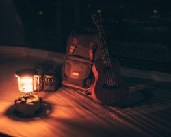 A gas lamp is on the tent floor at night and a bag with a ukulele and shoes next to it. Camping equipment, vocation and travel concept.